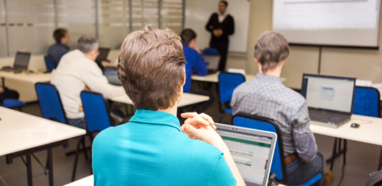 Rear view of trainees listening to their instructor and doing practical tasks on their laptops.