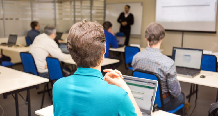 Rear view of trainees listening to their instructor and doing practical tasks on their laptops.